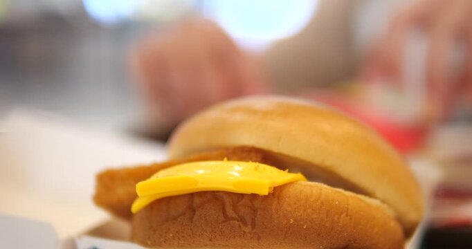 Close-up cinematic shot of a delicious crispy fish burger with melted yellow cheese on a soft bun, fast food and appetizing meal concept