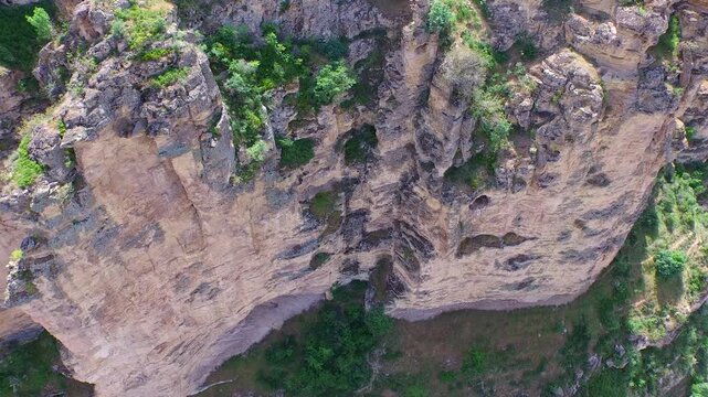 Aerial view of vertical karst limestone cliff wall with eroded rock layers and sparse vegetation. Camera looks straight down while moving sideways creating cinematic geological texture depth.