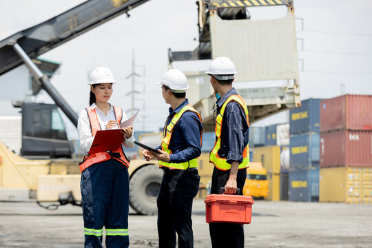 Three workers in safety gear discuss logistics at a busy shipping port with containers and heavy machinery in the background.