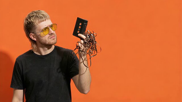 Conceptual generation gap: Confused Gen Z young man trying to understand an audio cassette tape.