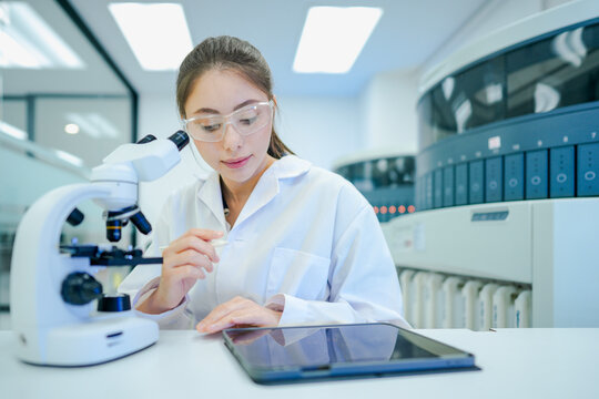 Digital pathologist integrating optical microscopy analysis with telepathology tablet interface. Female scientist digitizing histological biopsy data in smart lab.
