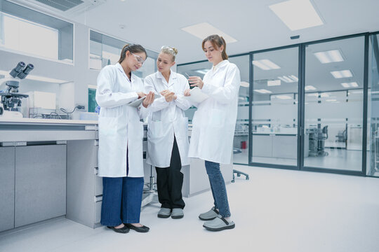 Diverse biotech research team analyzing experimental data metrics on digital tablet. Female scientists discussing strategic r&d protocols in modern laboratory.