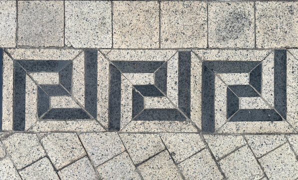 Close up of outdoor paving stone tiles in meander or greek key pattern. With black and beige color. For outdoor pavement, classic sidewalk. Seamless background texture