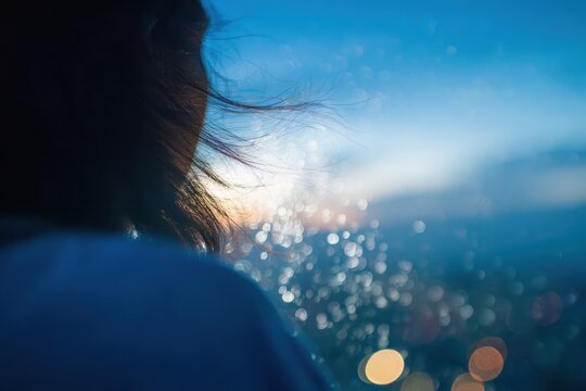 窓の外に輝く街の明かりを眺める人