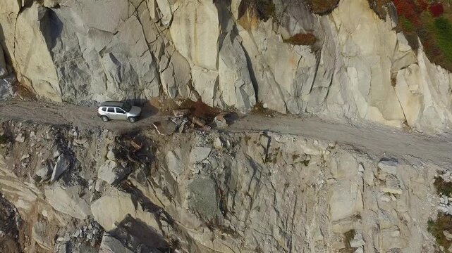 Aerial view of stranded 4x4 SUV on dangerous mountain road blocked by landslide near cliff. Rugged landscape, wilderness, rockslide, and aviation express solo airsport action in minimal composition.