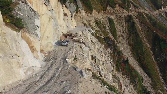 Aerial view of stranded 4x4 SUV on dangerous mountain road blocked by landslide near cliff. Rugged landscape, wilderness, rockslide, and aviation express solo airsport action in minimal composition.