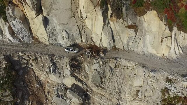 Aerial view of stranded 4x4 SUV on dangerous mountain road blocked by landslide near cliff. Rugged landscape, wilderness, rockslide, and aviation express solo airsport action in minimal composition.