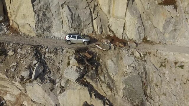 Aerial view of stranded 4x4 SUV on dangerous mountain road blocked by landslide near cliff. Rugged landscape, wilderness, rockslide, and aviation express solo airsport action in minimal composition.