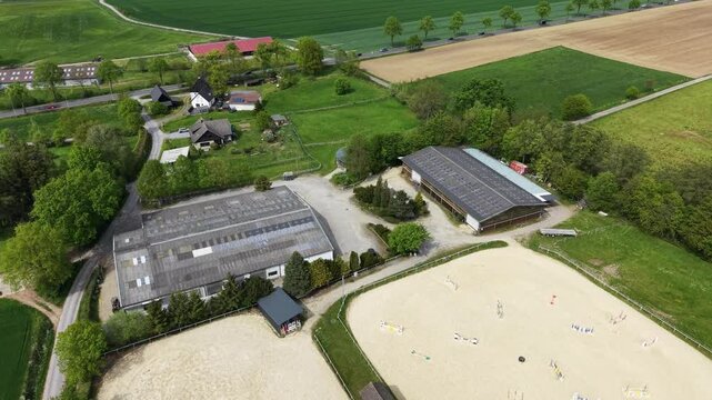 High-angle drone shot flying over an equestrian center with riders practicing in sand arenas