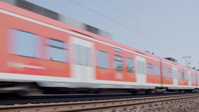 Red Passenger Train Speeding Along Railway Tracks Beside Lush Greenery on Sunny Day