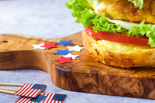 Close up bagel sandwiches on a cutting board with festive decorations, filled with crispy chicken, lettuce, and tomato on a gray background. American holiday concept and healthy morning routine.
