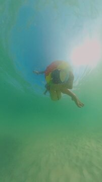 Vertical video. Underwater View Woman Holding Inflatable Ring With Person Sitting Inside, Sunlight Flare Near Surface, Wide Angle Perspective, Clear Tropical Water, Summer Activity