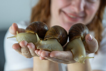 doctor holding giant achatina snail in her palm looking away with calm expression in clinical environment wearing white uniform and stethoscope concept of veterinary, cosmetology, medicine © Lana Pietukhova