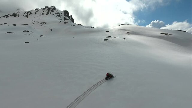 Aerial tracking view of a lone rider crossing pristine snowfields on a snowmobile in the Pyrenees. Alpine terrain, exploration, wilderness, and cantabrian suggest adventure leisure and freeflight.