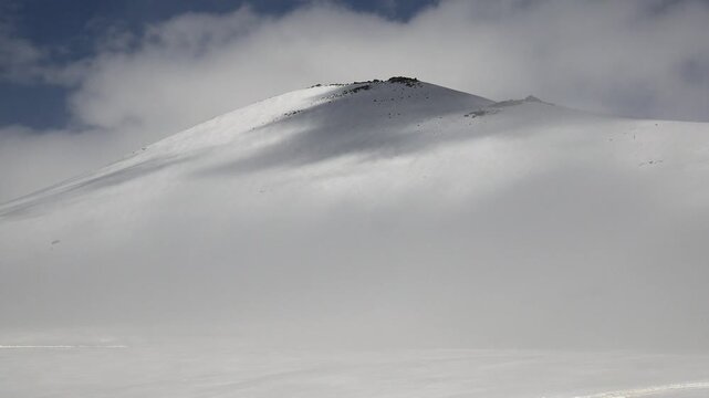 High altitude treeless snowy mountain slope in the Pyrenees with untouched snow and cloud motion. Winter mountains, alpine terrain, dark clouds, white landscape create moody atmospheric drama.