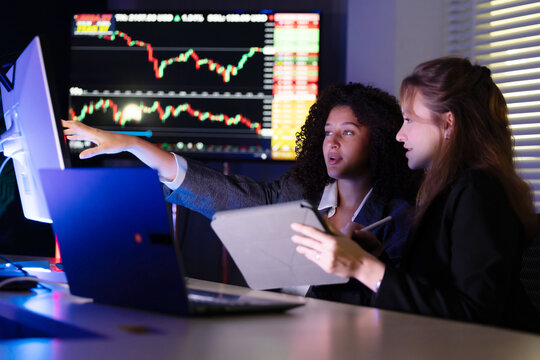 Colleagues discuss stock market trends in a modern office setting during evening hours