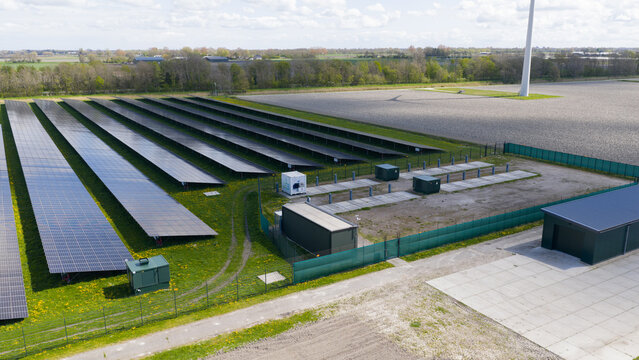 Aerial view of rows of solar panels in a solar farm surrounded by green fields and trees under a bright sky Warmenhuizen, North Holland, Netherlands.