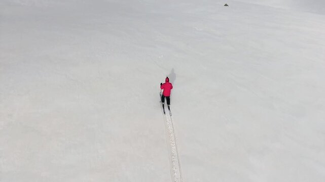 Lone skier descends rocky snow covered mountain during winter wearing vivid red jacket. Rugged terrain, alpine slope, exploration, and adrenaline express solo airsport action in minimal composition.