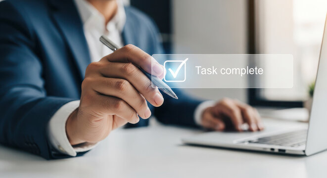 Business professional completing task on laptop, holding pen with digital checkmark overlay indicating task completion in modern office setting