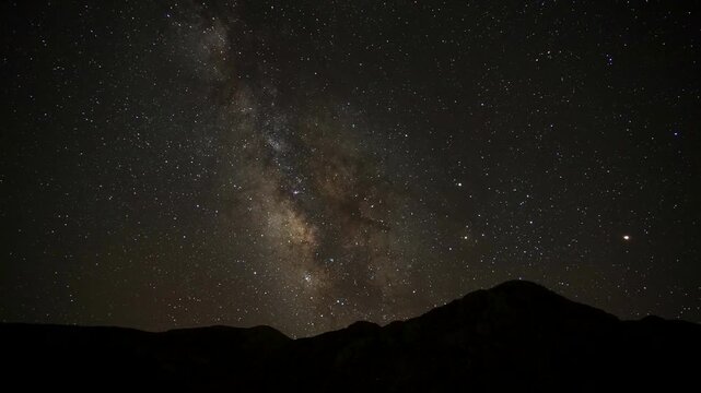 Time lapse of starry night sky above rugged mountain silhouettes beneath clear dark heavens. Alpine peaks, peaceful landscape, and astrophotography create tranquil cosmic atmosphere and science value.