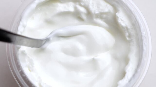 Stirring yogurt in a plastic cup with a spoon on a white table. Fermented dairy product. Concept of healthy breakfast. Top view