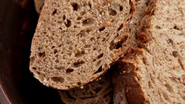 Top view of traditional German multigrain bread slices with seeds and fresh crust in a rustic wooden bowl. Rotation