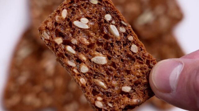 Close-up of a hand holding a crunchy dark rye rusk with sunflower seeds