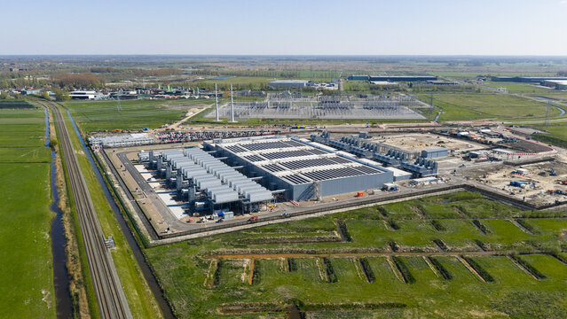 Aerial view of Datacenter Westpoort featuring large industrial cooling units and surrounding green fields with a railway track in Groningen, Groningen, Netherlands.