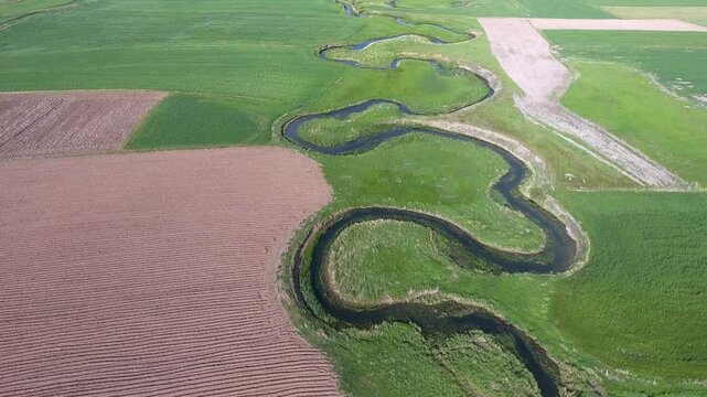 Aerial view of river meander flowing through agricultural fields on a flat plain in France. Spring season, rural plains, and watercourse support rural farming themes and seasonal production.