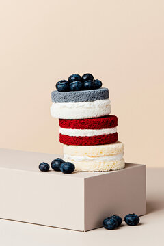 Stacked round cakes with blueberries on top on a beige plinth in a minimal studio composition.
