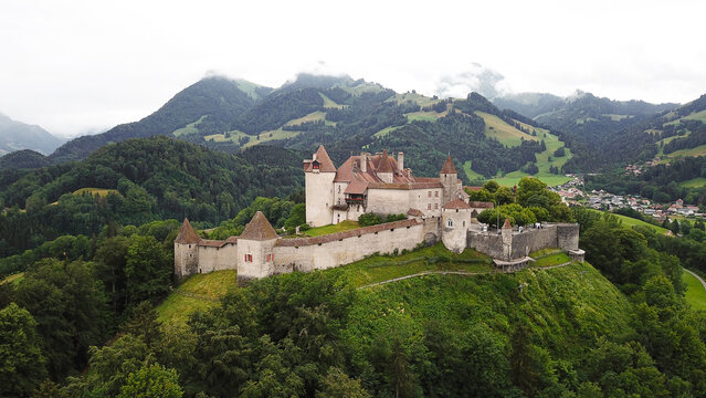Aerial view of the medieval Chateau de Gruyeres with its stone walls and towers on a green hill with the Swiss Alps and misty forests in the background Gruyeres, Fribourg, Switzerland.