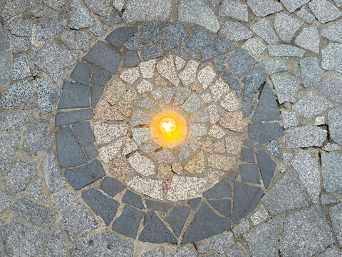 Natural random cut grey flagstone flattened on a surface with round circle medallion shape and fire lit in the middle. For outdoor floor or wall finishes in campire