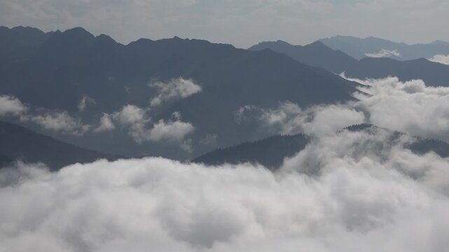 Sea of clouds and fog covering valleys between high altitude mountain peaks in landscape. Natural phenomenon with thick cloud layer blanketing mountainous terrain creating view.