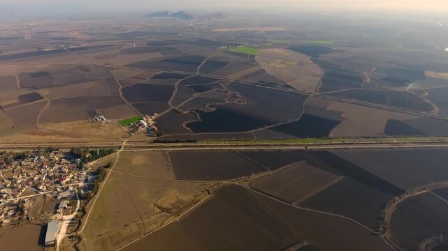 Aerial view of village houses and dirt field roads across flat brown alluvial plain. Rural settlement patterns with farmland paths and agricultural landscape textures.