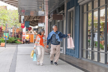 Naklejka premium Senior asian couple walking with shopping bags at mall smiling and laughing, love retirement lifestyle, shopping happiness and active senior living, purchase sale promotion, retail therapy