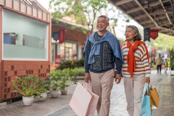 Naklejka premium Senior asian couple walking with shopping bags at mall smiling and laughing, love retirement lifestyle, shopping happiness and active senior living, purchase sale promotion, retail therapy