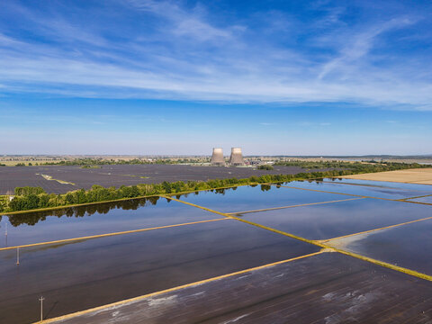 Aerial view of Tenuta Colombara flooded rice fields reflecting the blue sky with cooling towers and a solar farm in the distance Livorno Ferraris, Piemonte, Italy.