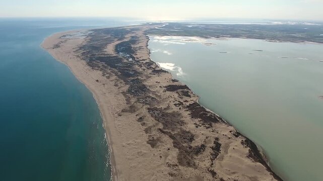 Aerial view of sandy longshore drift sands forming barrier between sea and calm lagoon. Coastal sediment shapes curved shoreline landscape with natural water separation.