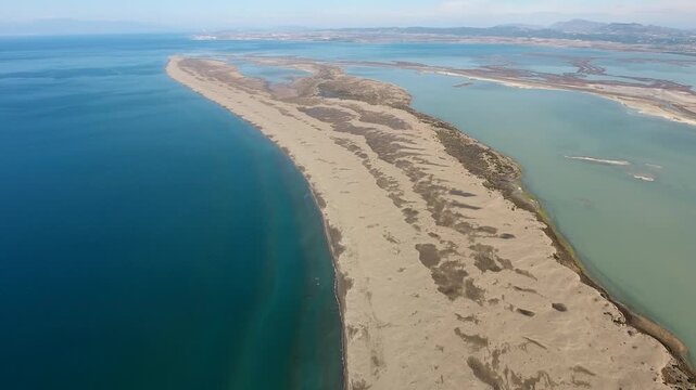 Aerial view of sandy longshore drift sands forming barrier between sea and calm lagoon. Coastal sediment shapes curved shoreline landscape with natural water separation.