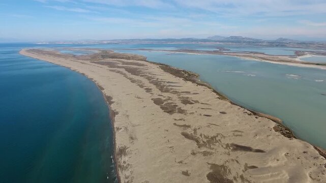 Aerial view of sandy longshore drift sands forming barrier between sea and calm lagoon. Coastal sediment shapes curved shoreline landscape with natural water separation.