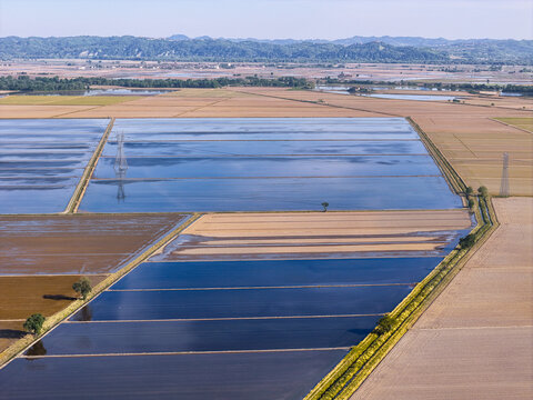 Aerial view of Tenuta Colombara with flooded rice fields reflecting the sky and geometric patterns across the rural landscape in Livorno Ferraris, Piemonte, Italy.
