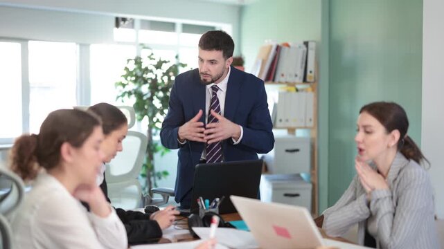 Young man stands at office desk and scolds group of upset women in office
