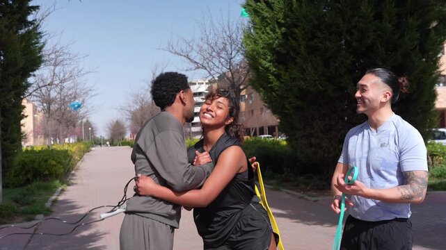 Three multicultural friends in sportswear laughing and greeting each other with hugs and high fives before working out together in a city park