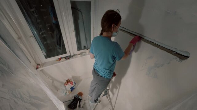 Woman plastering wall corner near window