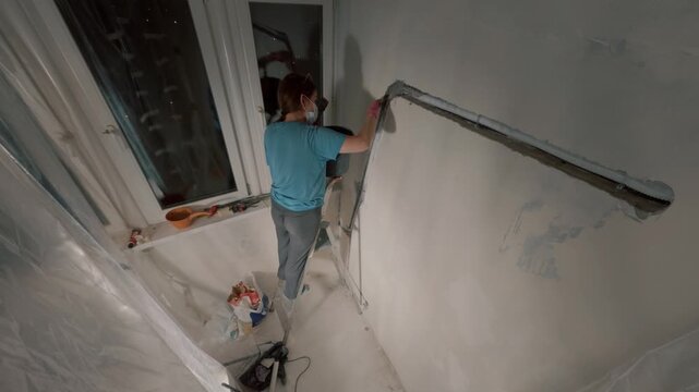 Female worker plastering wall corner near window