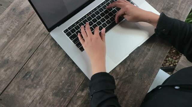 Top View of Hands Typing on Laptop with Coffee and Plants on Wooden Desk