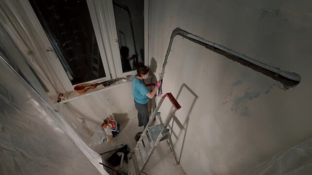 Worker plastering wall corner near window with roller