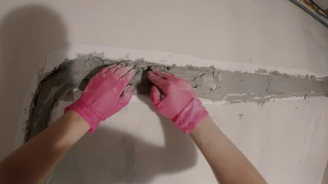 Hands applying plaster to wall corner crack