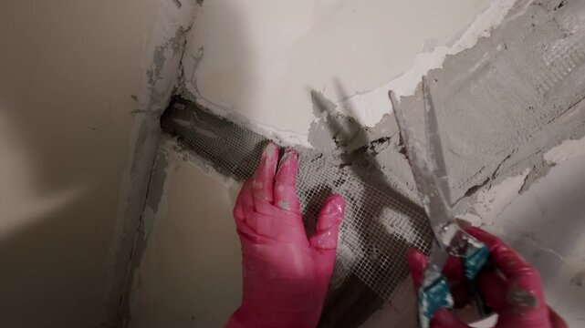 Applying plaster to wall corner with tools and gloves