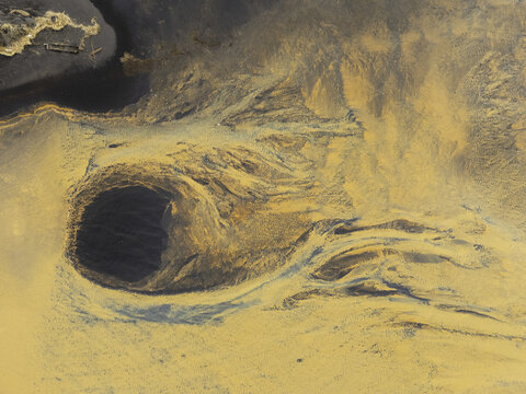 Aerial view of abstract patterns of orange sediment and a dark circular pool in a glacial river delta in Hallgeirseyjarvegur, Rangarthing eystra, Iceland.